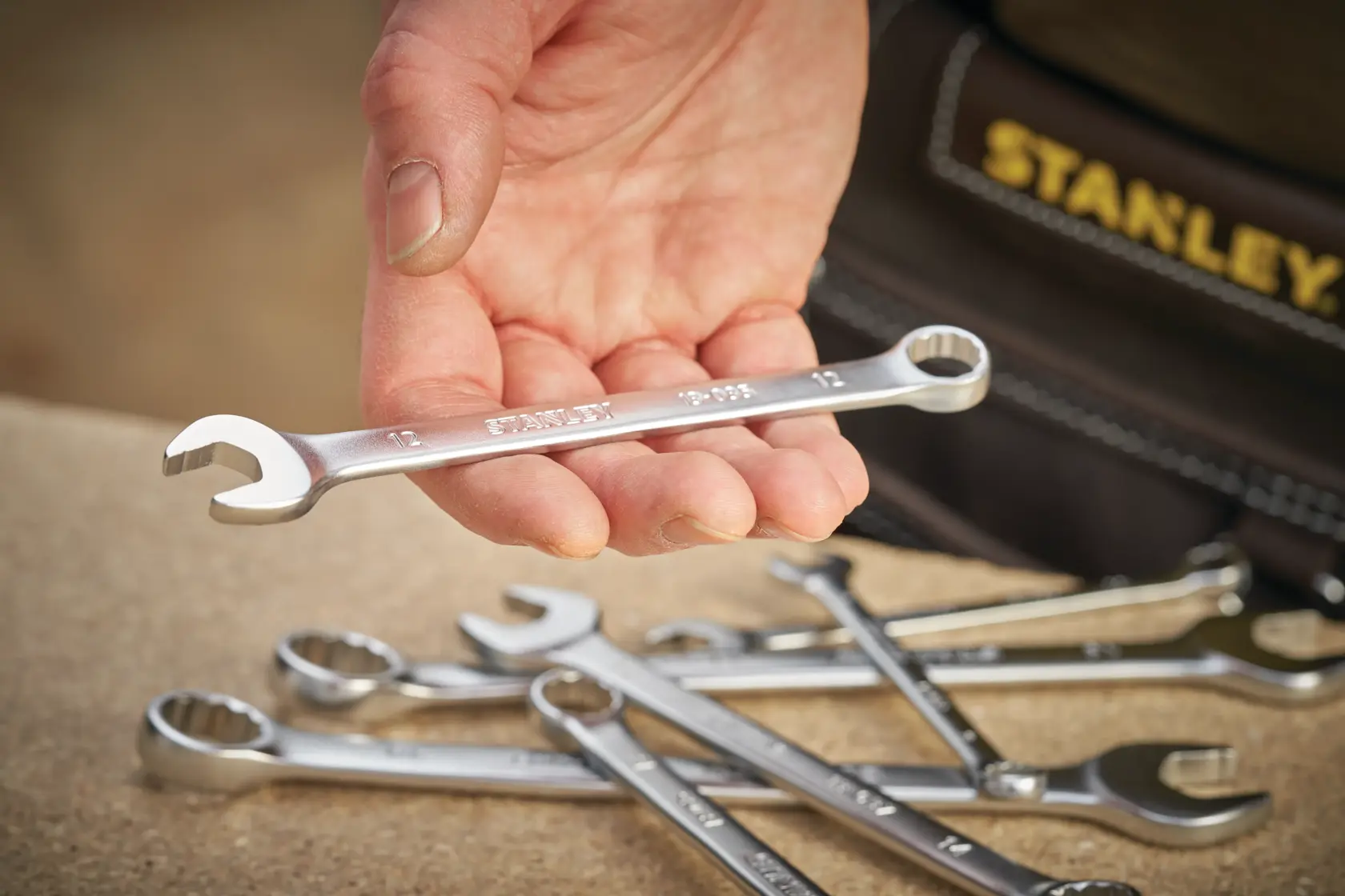 STANLEY FMMT13030-0 combination wrench held in hand, several wrenches on tabletop, close-up photography.