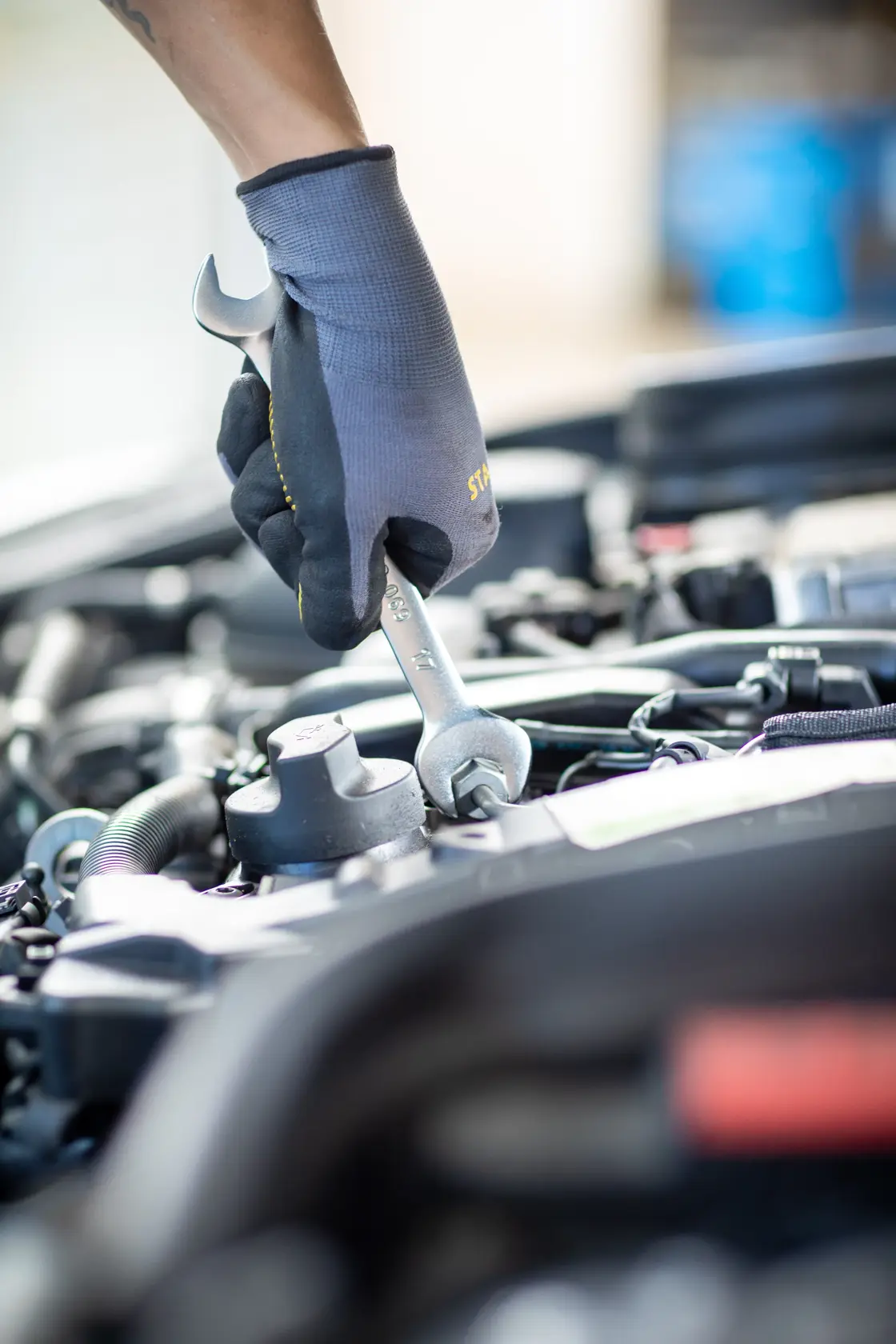 Photo of STANLEY FMMT13074-0 wrench in gloved hand tightening bolt on car engine, close-up.
