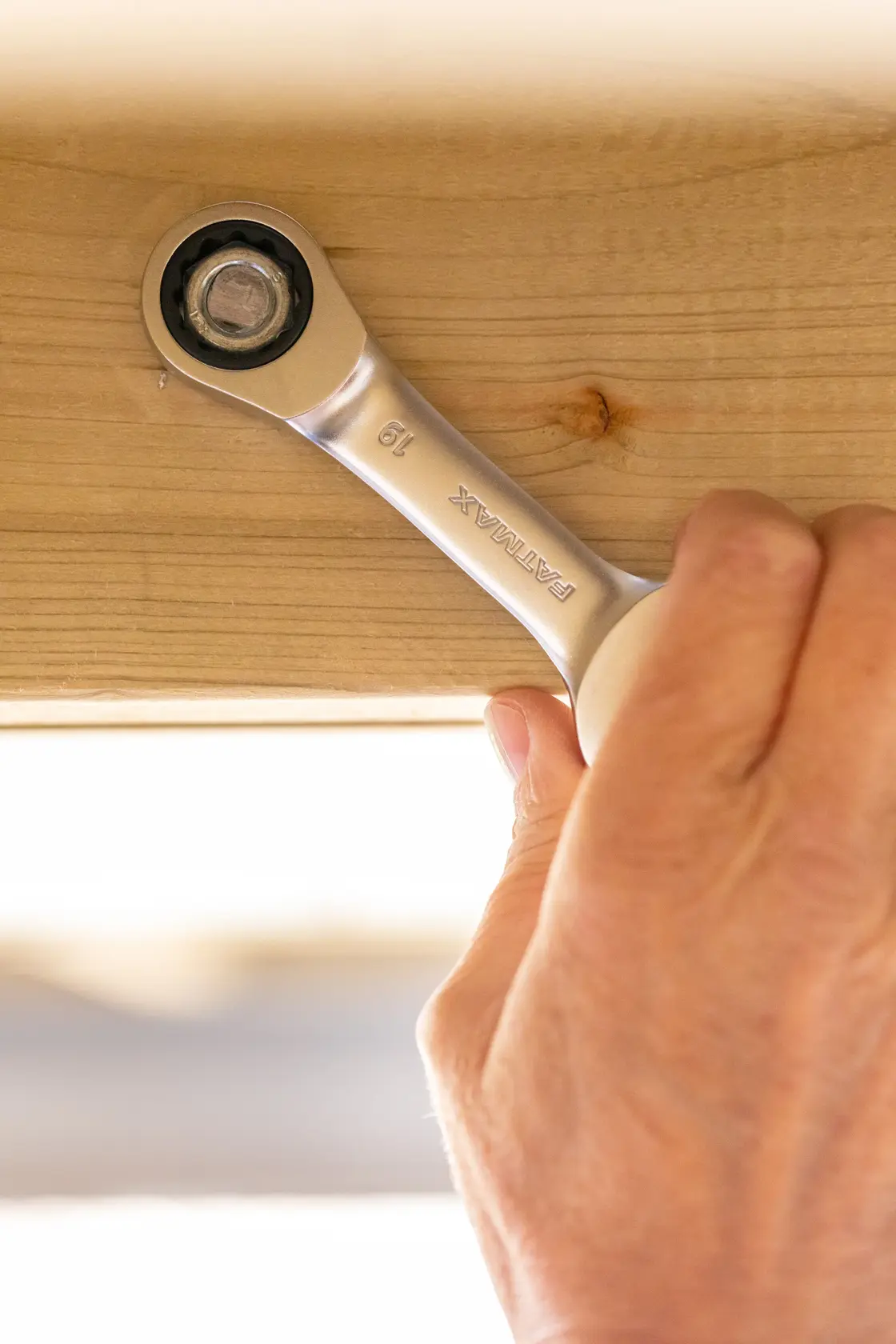 STANLEY FMMT13098-0 ratcheting wrench tightening bolt on wood beam, close-up view, photography product.