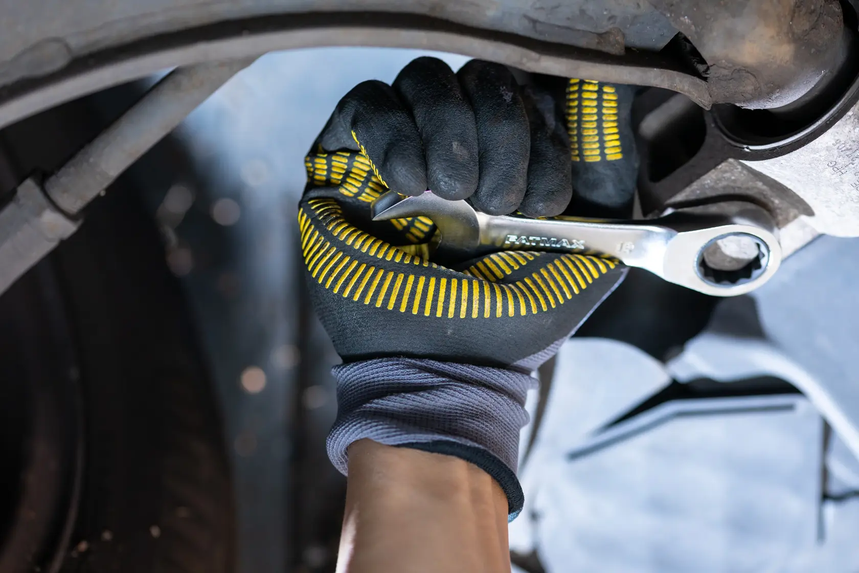 STANLEY FMMT13115-0 ratchet spanner in gloved hand tightening bolt on car part, close-up action photo.