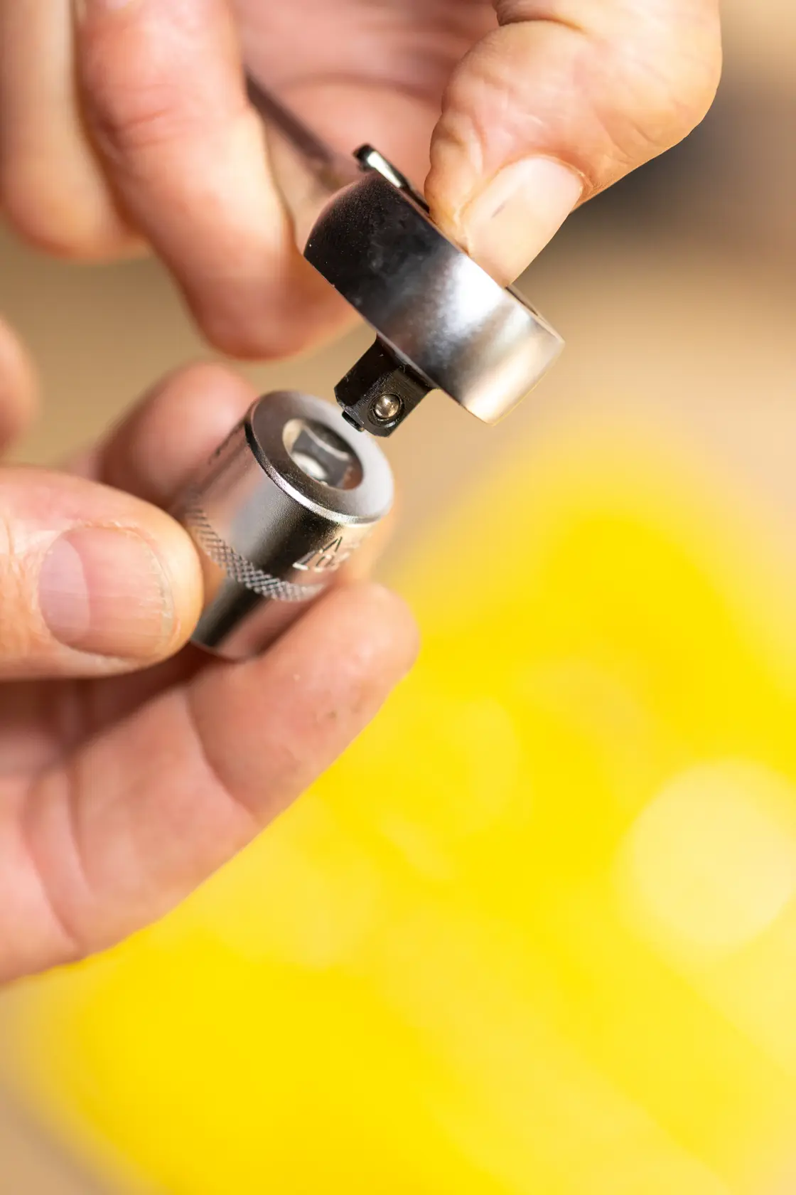 Close-up photo of hands connecting STANLEY FMMT17194-0 ratchet and socket tool over yellow background.