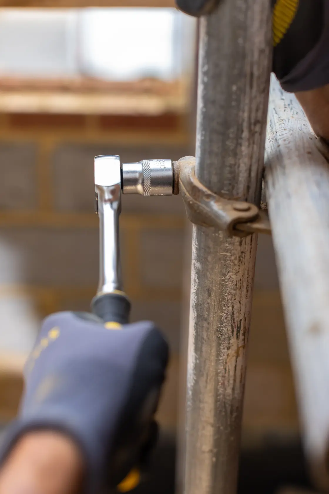 Photo of STANLEY FMMT17208-0 ratchet wrench tightening metal pipe joint, close-up with gloved hand.