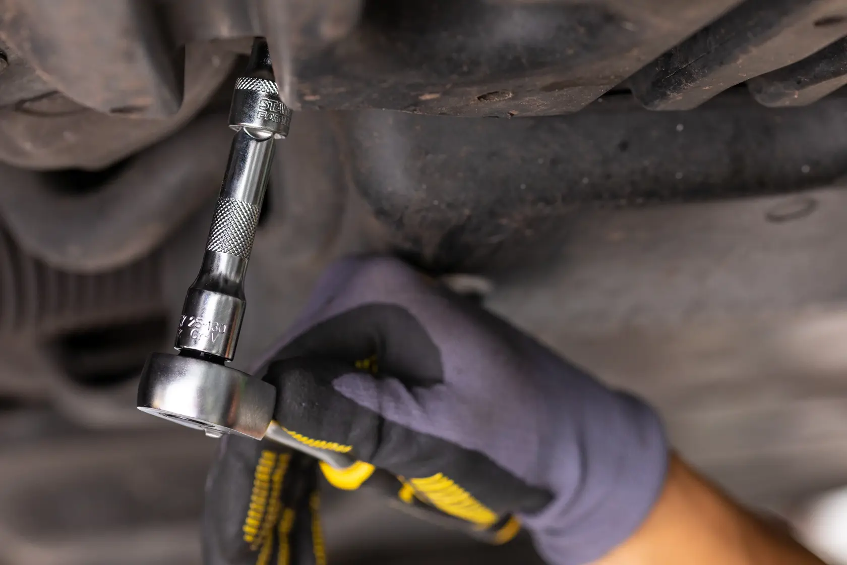 Photo of STANLEY FMMT25122-0 ratchet wrench being used under a car, gloved hand turning tool.