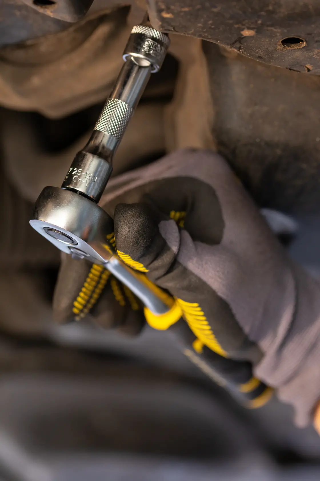 STANLEY FMMT25123-0 ratchet wrench in use, close-up, held by gloved hand under vehicle.