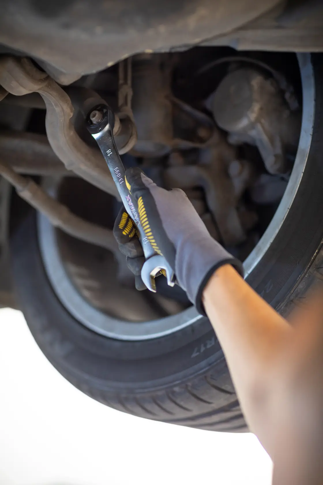 STANLEY FMMT82849-0 combination wrench used on car suspension, close-up showing gloved hand and tire.