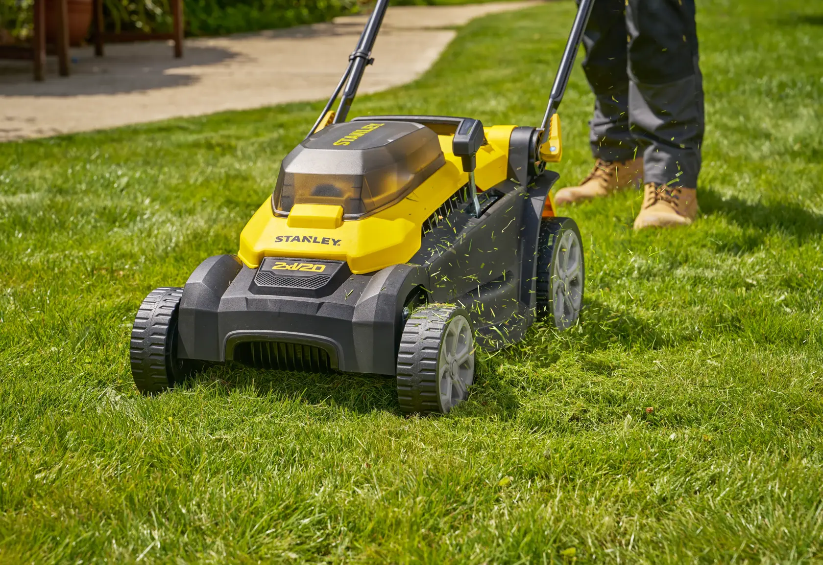 Photo of STANLEY SCMWP3701M2 lawn mower on grass, yellow and black cordless model with person mowing.