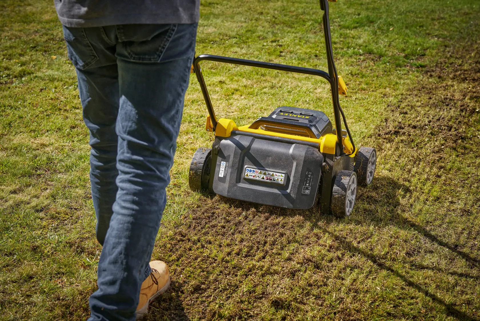 STANLEY SCOEP3801N lawn scarifier in use, rear view, with person aerating a grassy lawn.