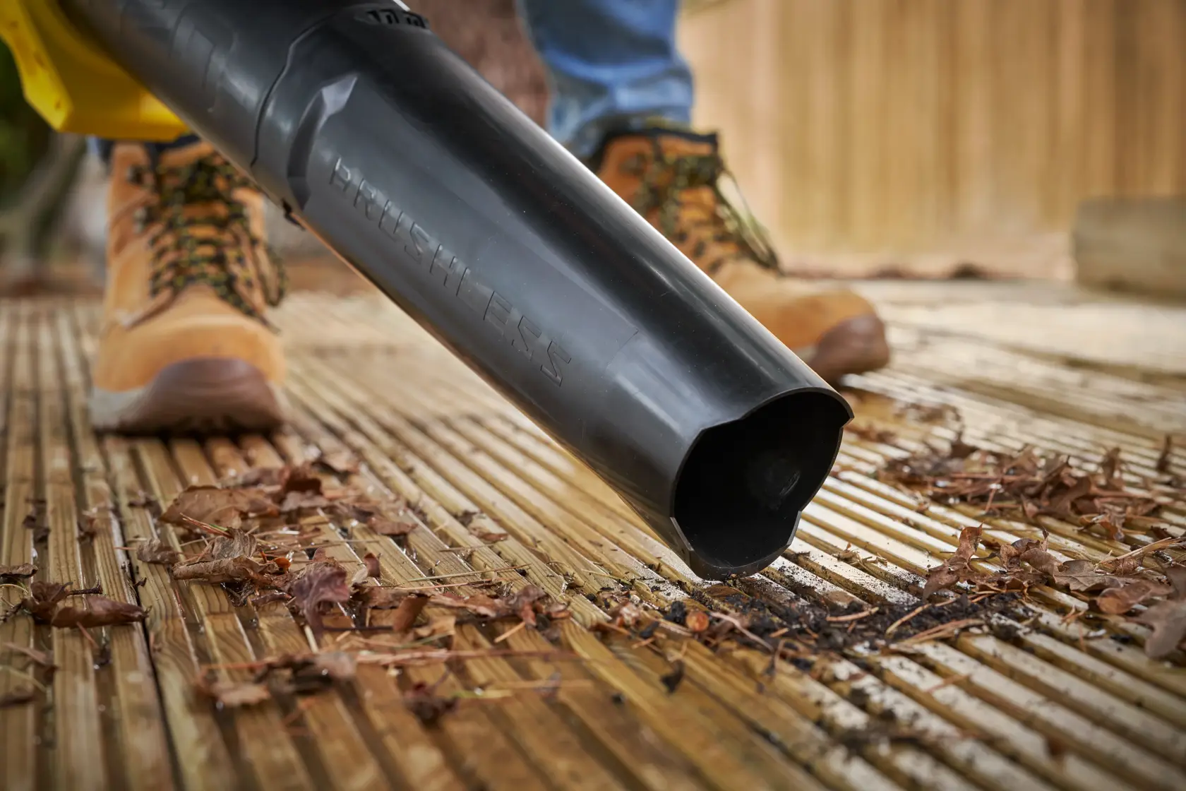 STANLEY SFMCBL730M1 leaf blower nozzle in use on wooden decking, blowing dry leaves and debris.