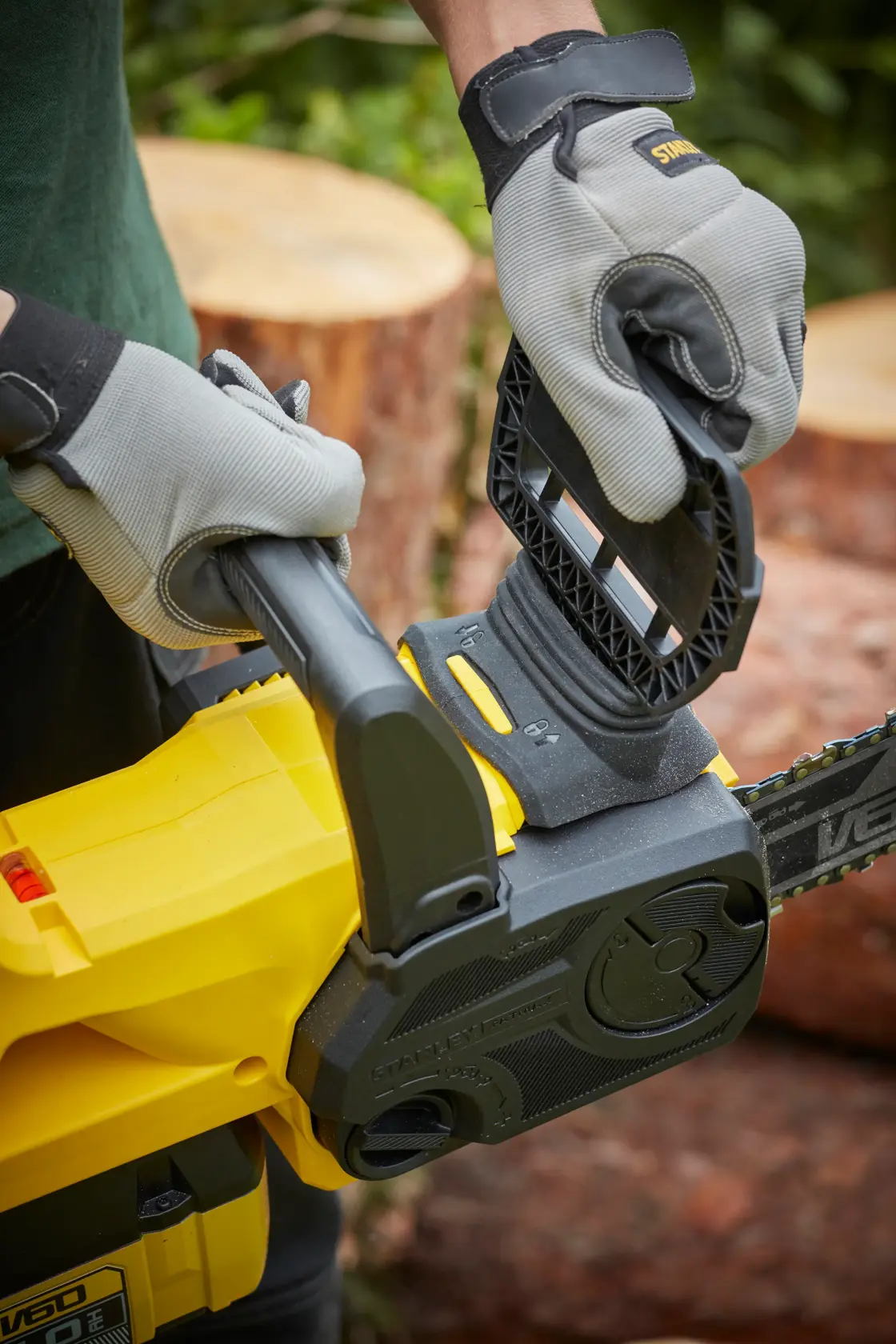 STANLEY SFMCCSB664B chainsaw close-up in use, user wearing gloves operating chain brake outdoors.