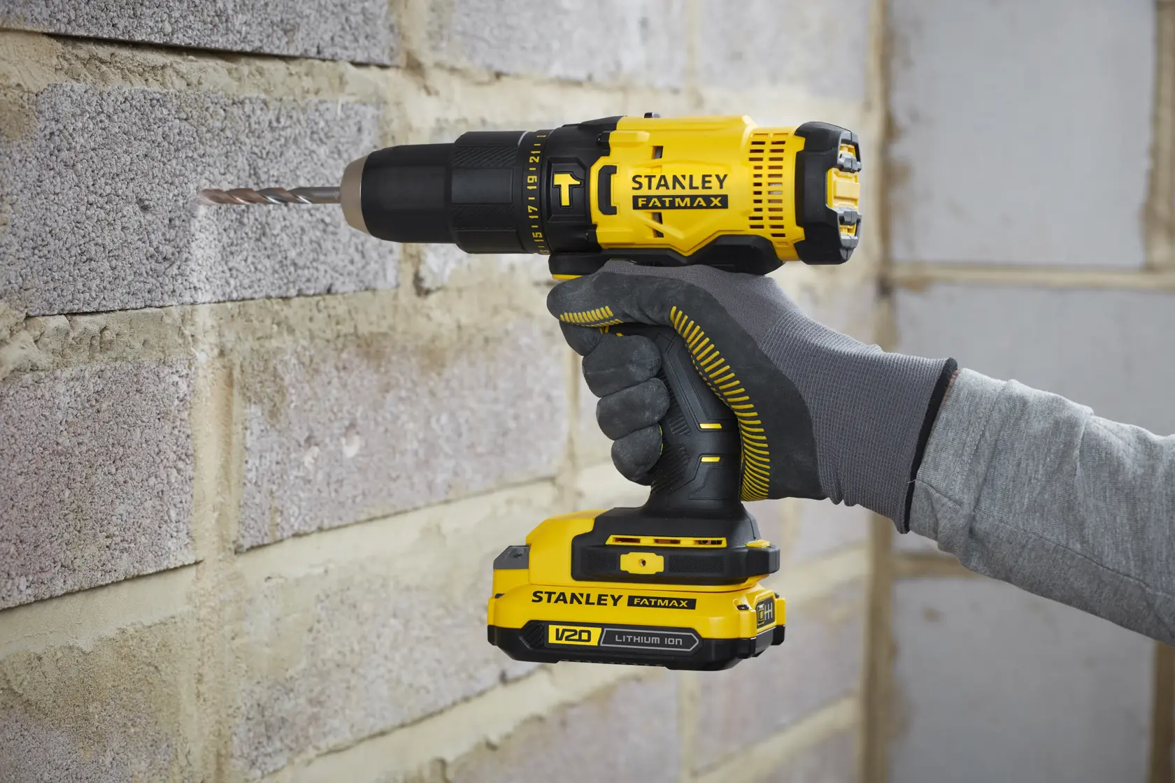 STANLEY SFMCD711C2K cordless drill in use, yellow and black, drilling into masonry wall.