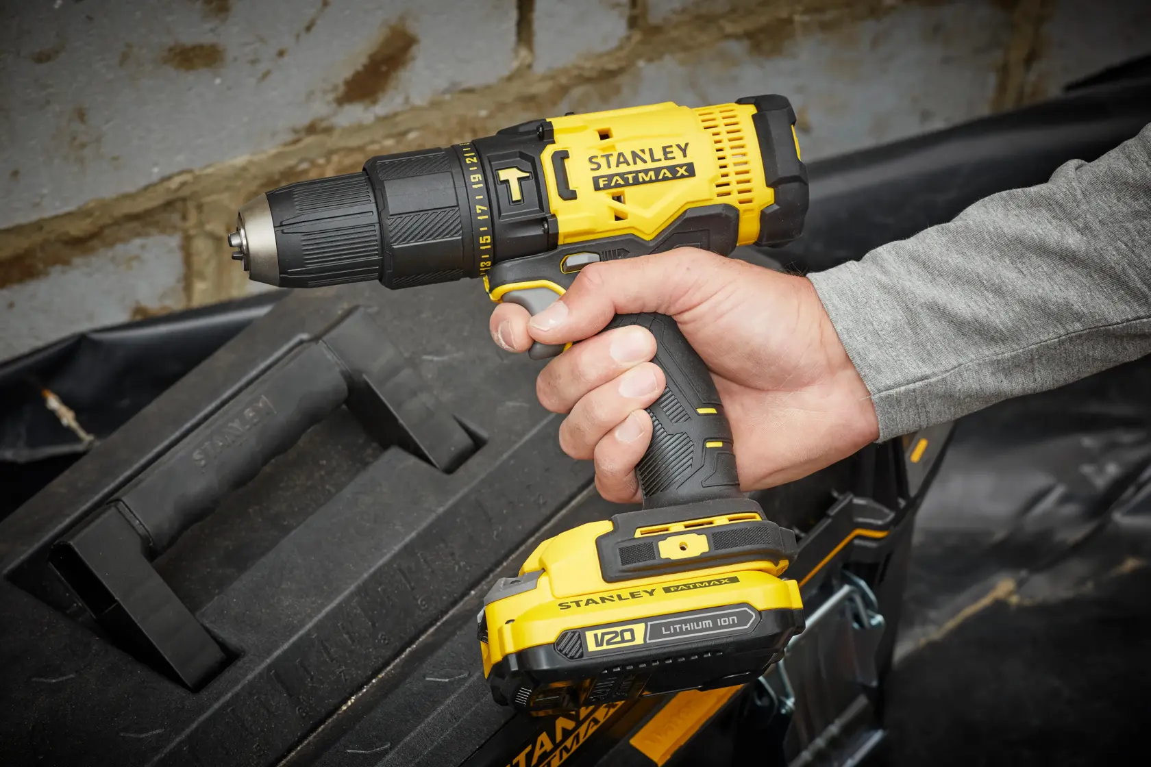 Photo of STANLEY SFMCD711C2S cordless drill, yellow and black, held in hand near tool box.