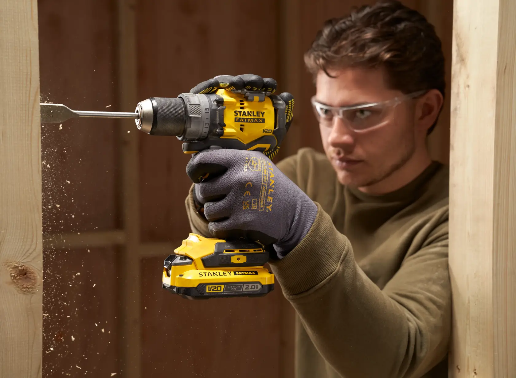Photo of STANLEY SFMCD725B cordless drill in use, drilling into wood, yellow and black design.