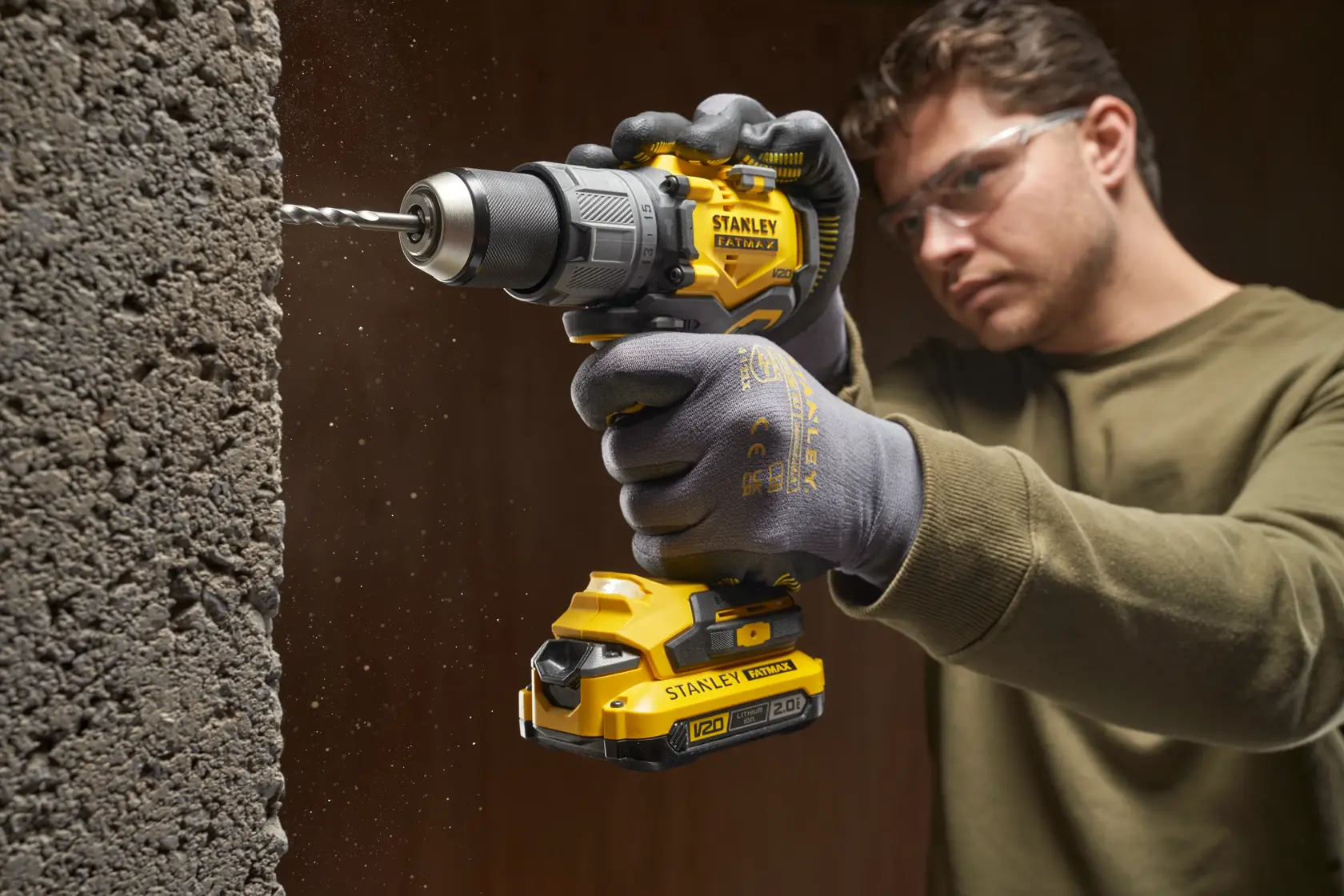Photo of STANLEY SFMCD726D2K cordless drill in use, drilling into concrete wall, visible V20 battery.