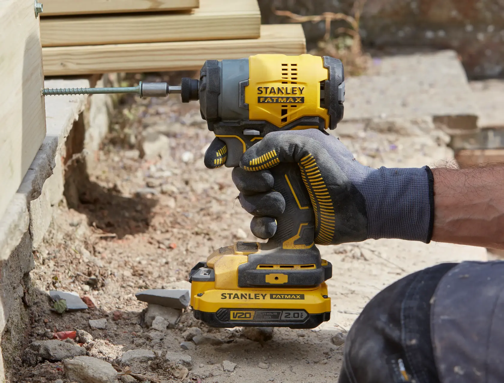 STANLEY SFMCF810D2K impact driver held by gloved hand, driving screw into wooden beam outdoors.