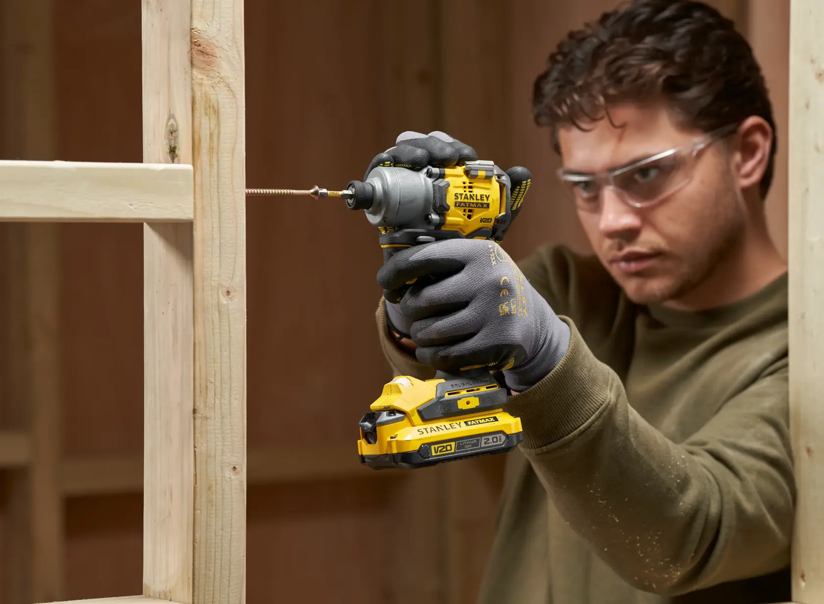 Photo of STANLEY SFMCF830B impact driver in use, driving screw into wooden frame, user wearing gloves.