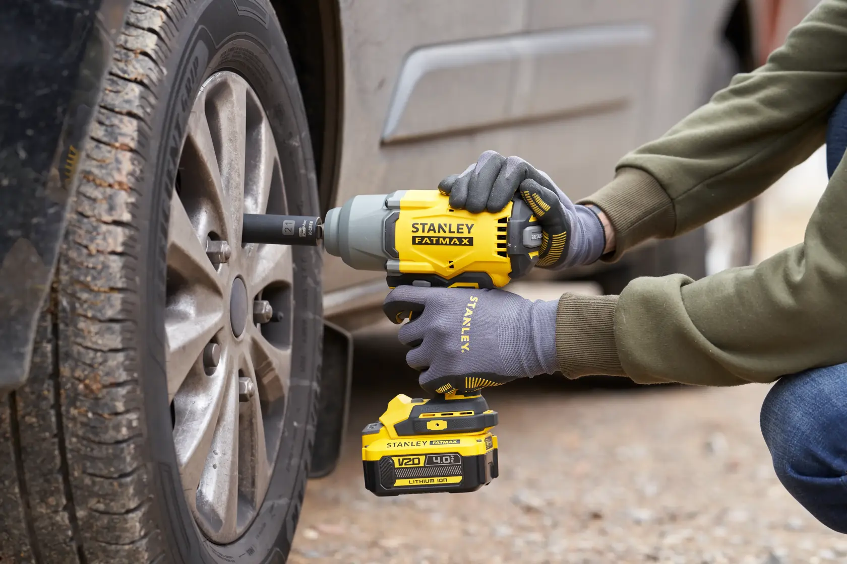 Photo of STANLEY SFMCF940M1 cordless impact wrench being used to tighten car wheel lug nuts outdoors.