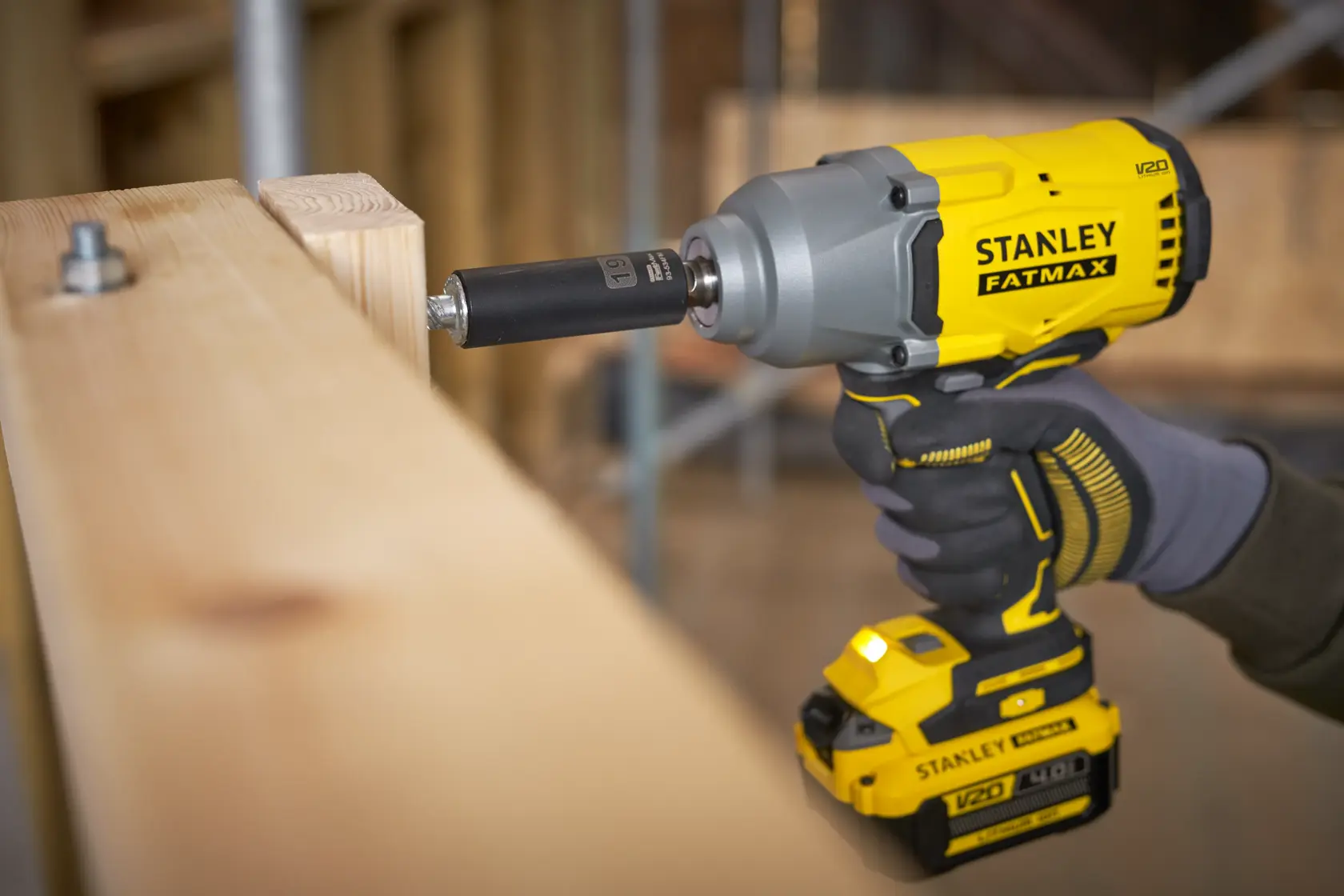Photo of STANLEY SFMCF940M1 cordless impact wrench being used to fasten a bolt on wooden beams, close-up angle.