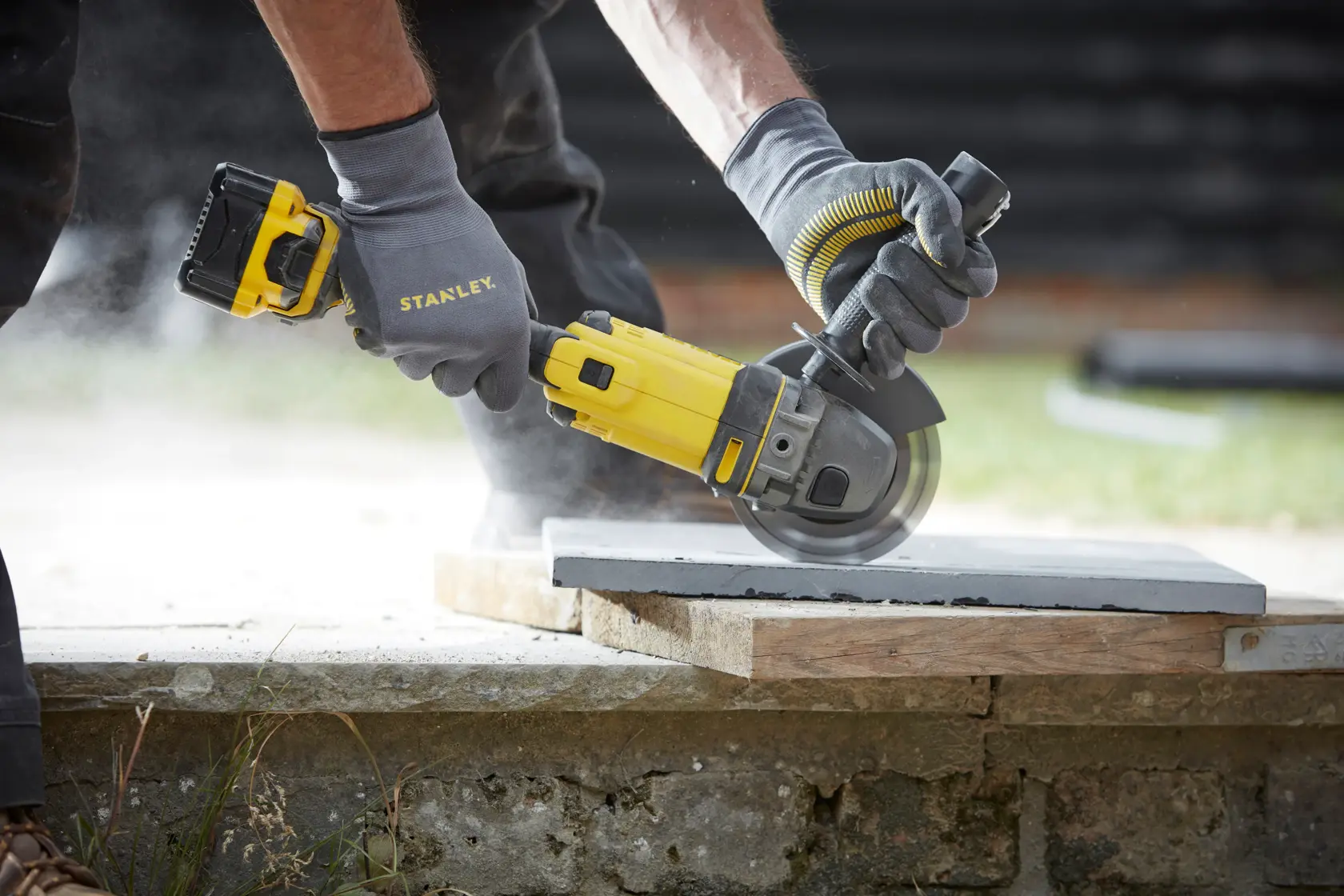 STANLEY SFMCG400M2K cordless angle grinder in use cutting concrete, close-up outdoors.