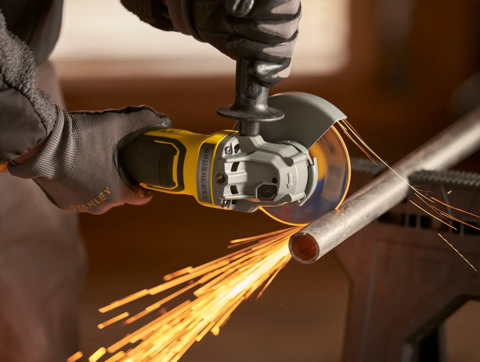 Stanley SFMCG700M2K grinder cutting metal pipe with sparks, close-up action shot.