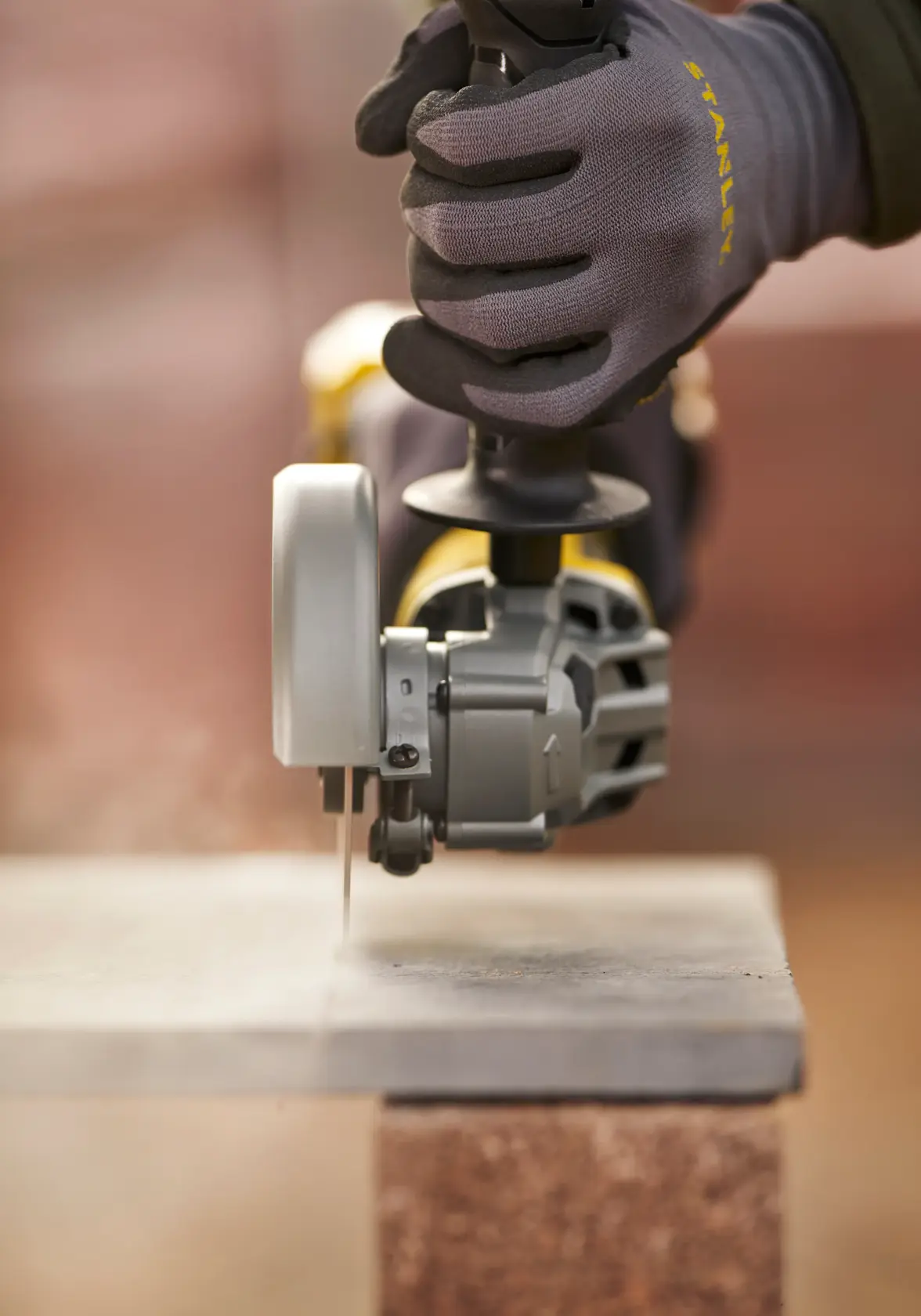 STANLEY SFMCG700M2K grinder cutting stone slab, angled view, worker wearing STANLEY gloves.