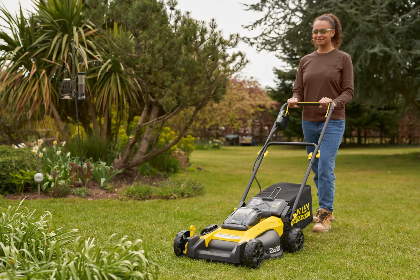Photo of STANLEY SFMCMW2651M lawn mower in use on grass, showing yellow and black design, garden background.
