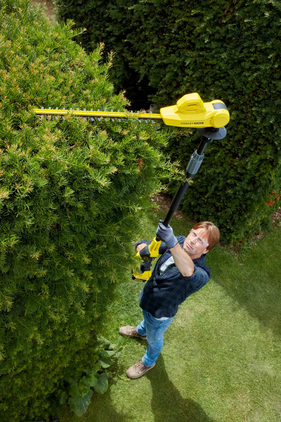 Photo of a person using STANLEY SFMCPH845M1 pole hedge trimmer to trim tall bushes outdoors.