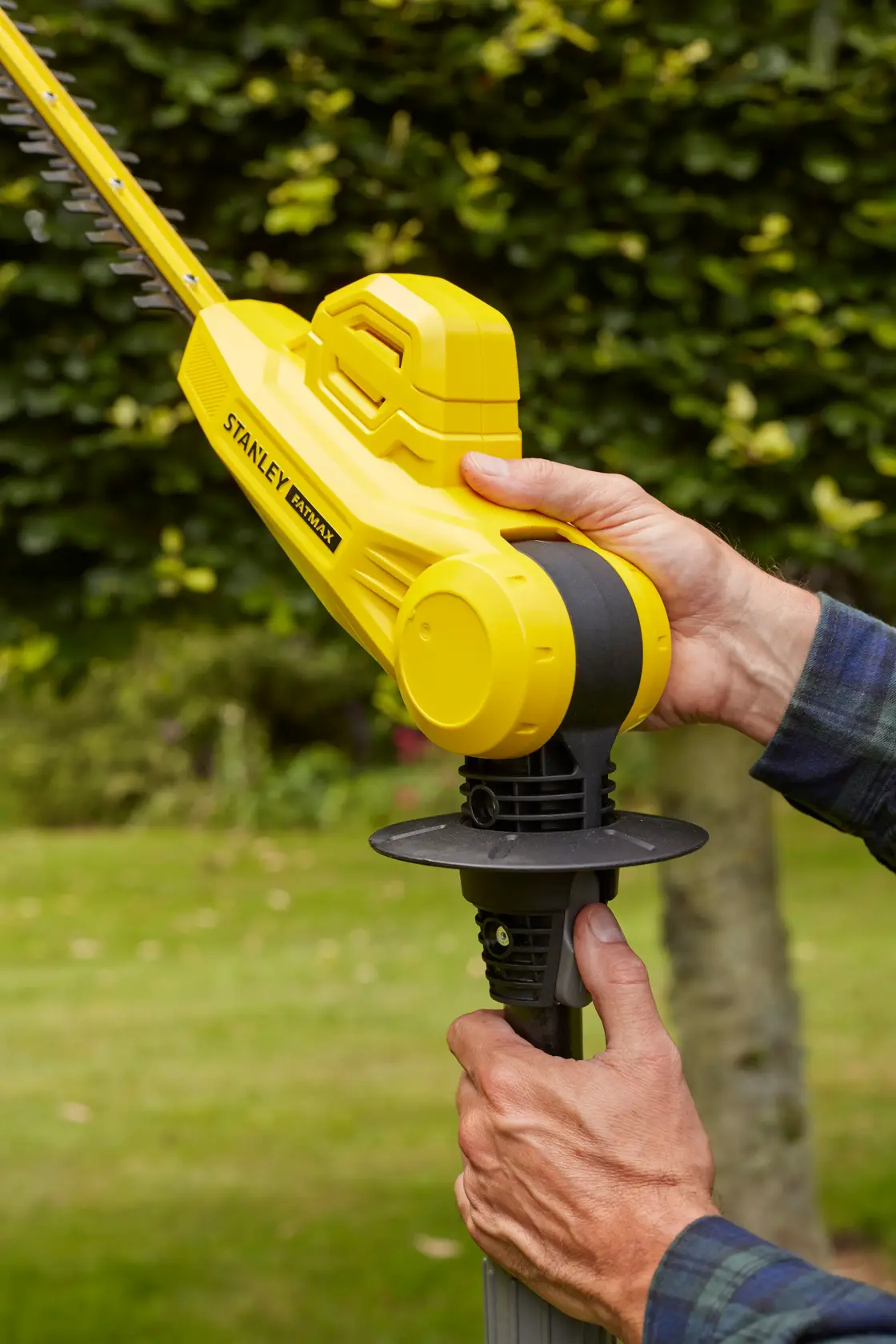 Photo of STANLEY SFMCPH845M1 yellow cordless hedge trimmer being held outdoors in a garden.