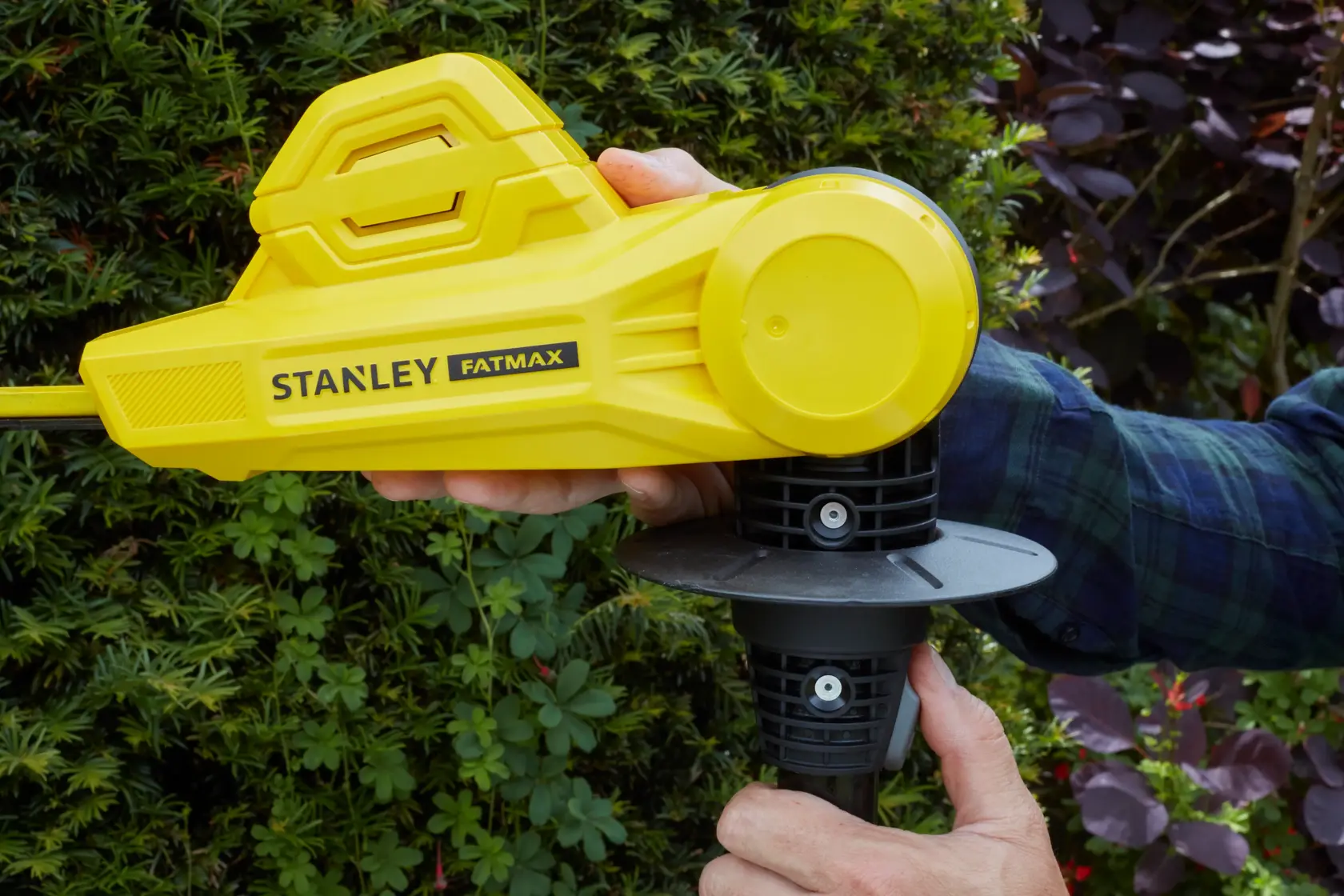 STANLEY SFMCPH845M1 yellow cordless hedge trimmer in use, close-up of handle and body with garden background.