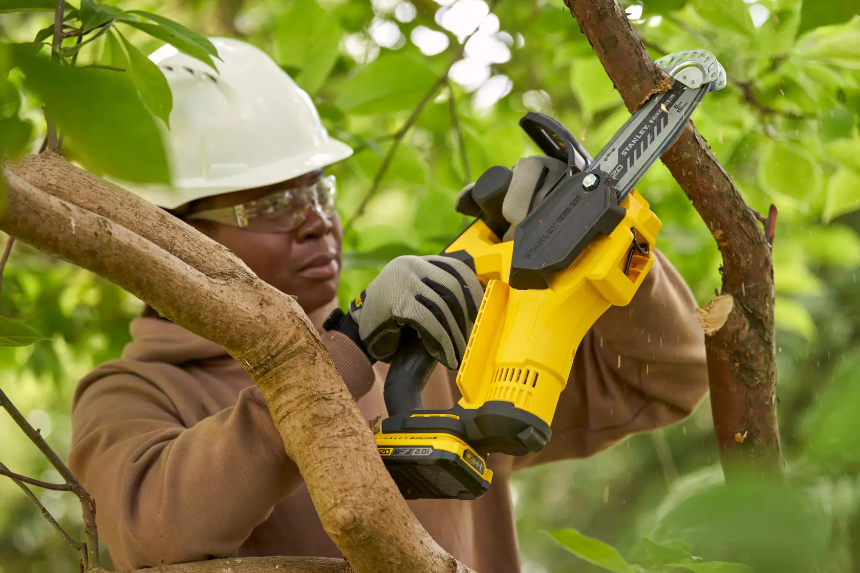 STANLEY SFMCPS415D1 cordless pruning saw cutting a tree branch outdoors, operator wearing gloves.