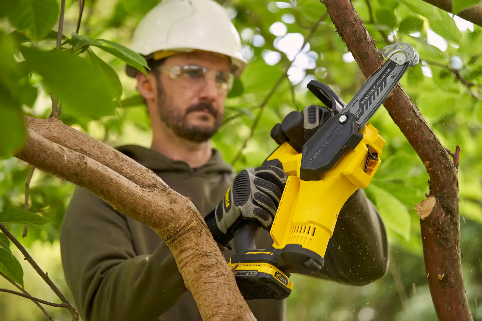 Stanley SFMCPS415D1 compact cordless chainsaw trimming a tree branch outdoors.