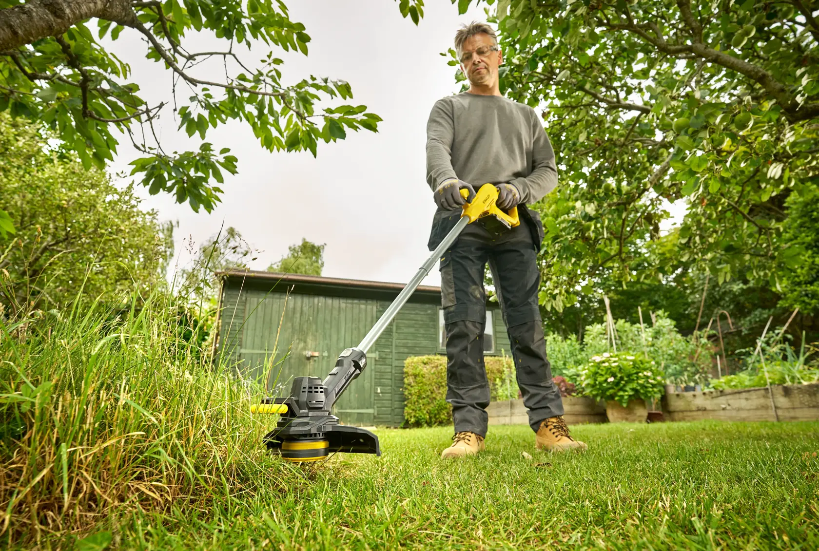 STANLEY SFMCST925B string trimmer in use by person cutting grass in a garden.