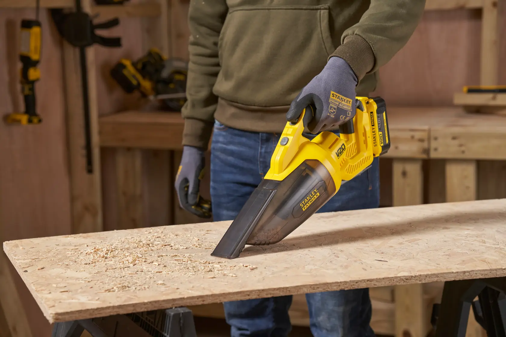 STANLEY SFMCVH001B handheld vacuum cleaner used to remove sawdust from a wooden board in a workshop.