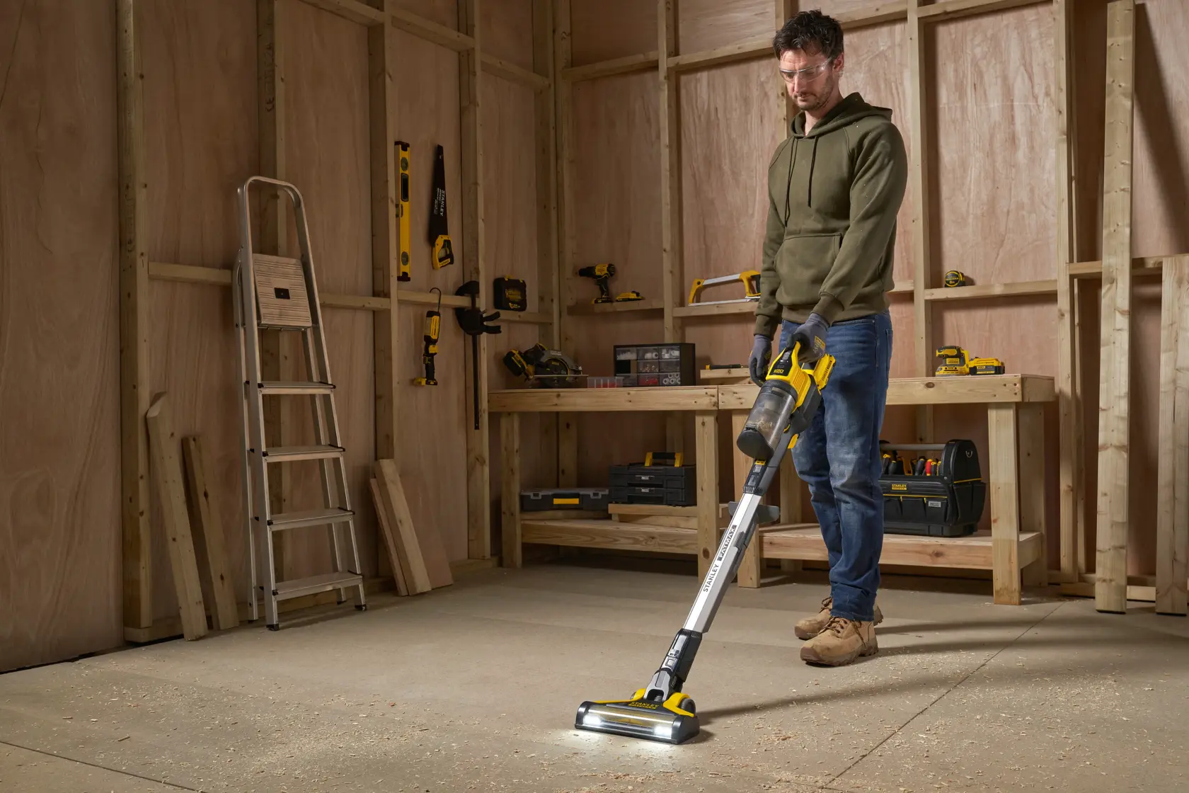 STANLEY SFMCVS001D1 cordless stick vacuum in workshop setting, cleaning sawdust from the floor.