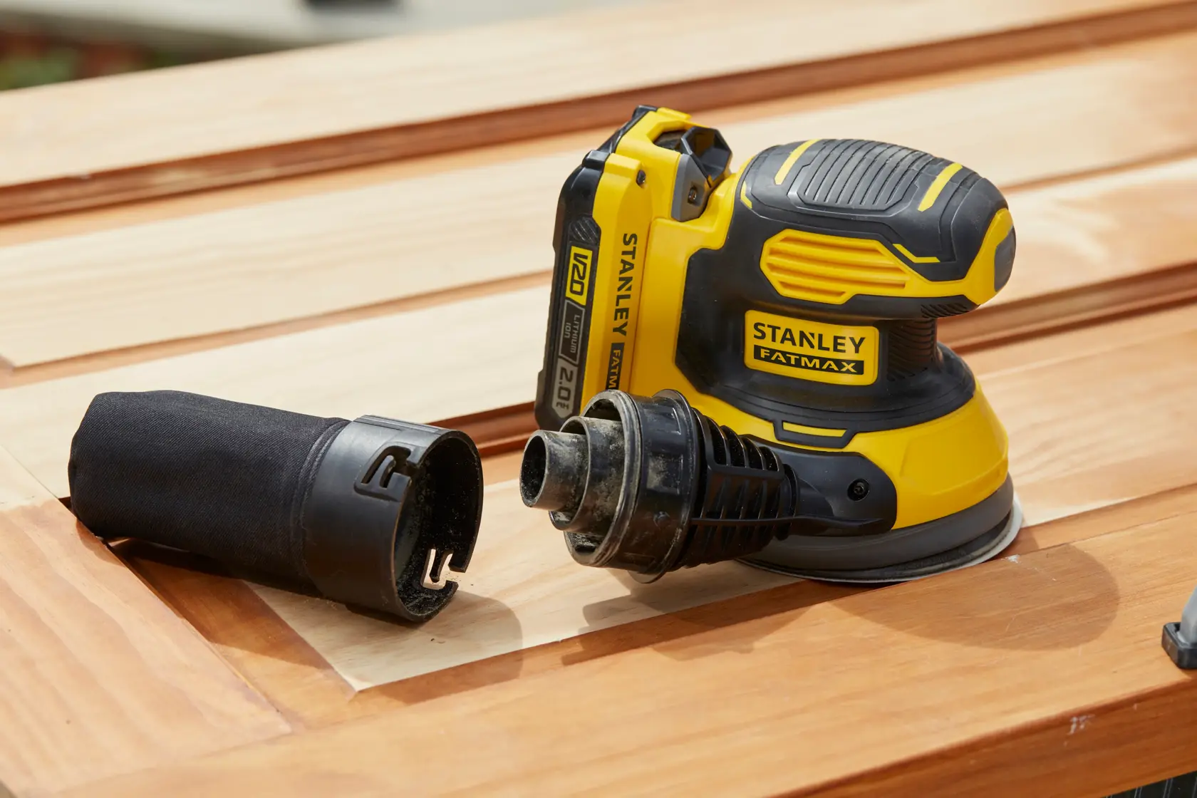 STANLEY SFMCW220D1S cordless sander on wood surface with dust collector detached, shown from side angle.