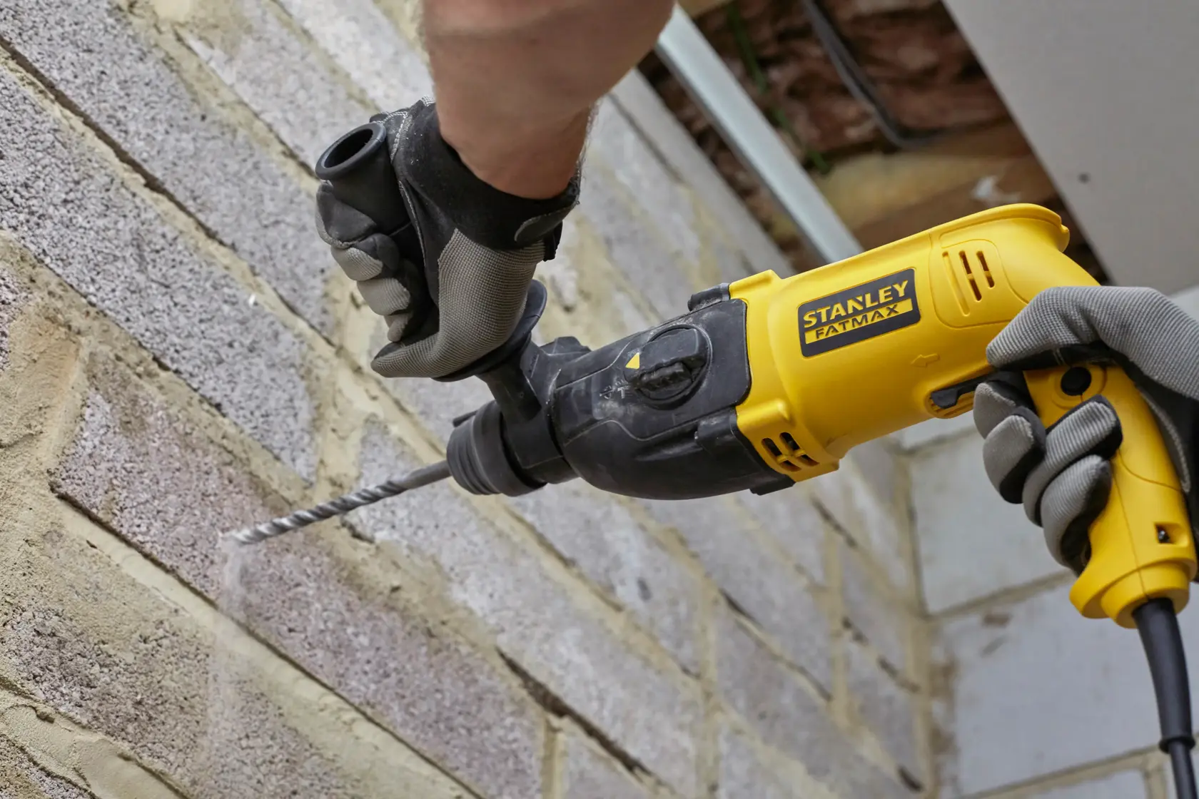 Photo of STANLEY SFMEH200K hammer drill in use on brick wall, yellow and black, product photography.