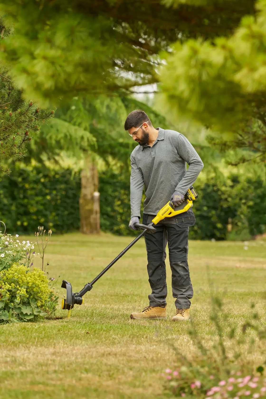 STANLEY STCST933B grass trimmer in use, person trimming lawn edge outdoors with yellow and black cordless tool.