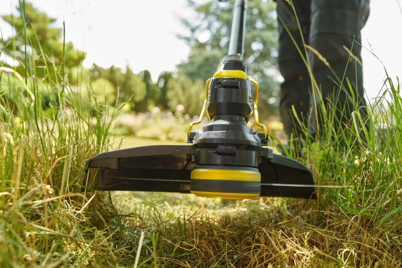 STANLEY STCST933B grass trimmer in use, close-up low angle view showing cutting head trimming tall grass outdoors.