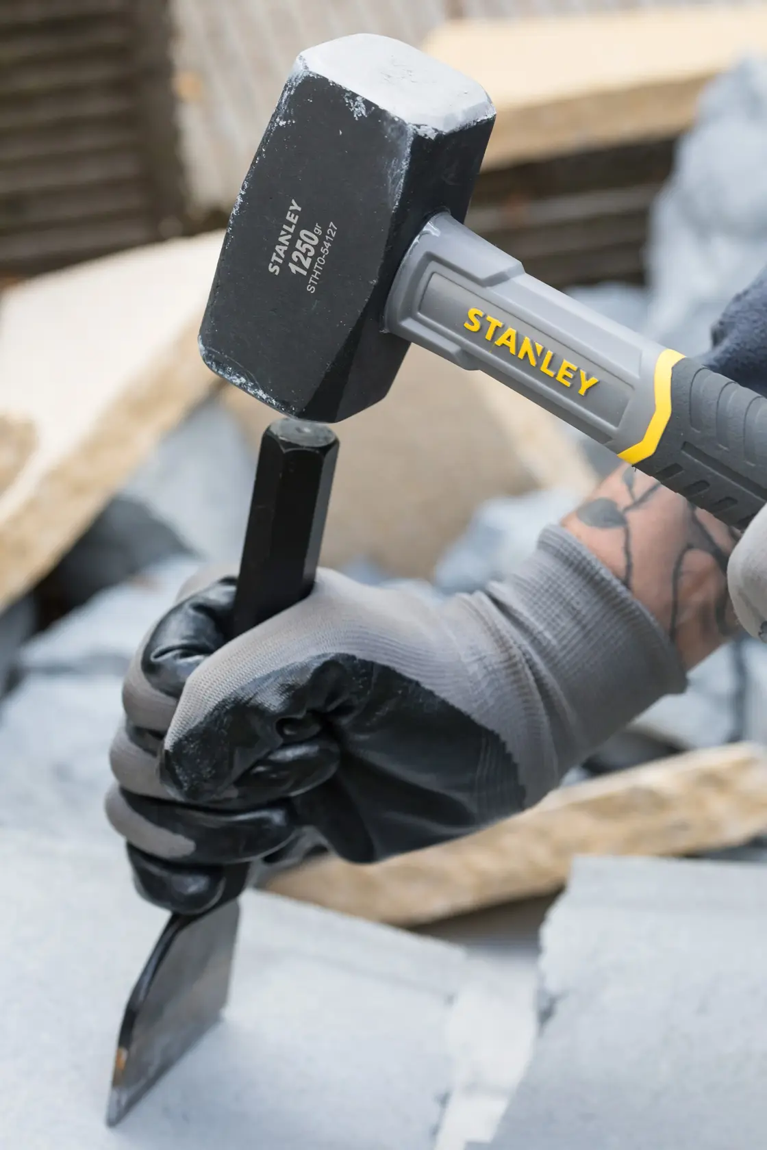 STANLEY STHT0-54127 sledge hammer being used with a chisel on stone, close-up view.
