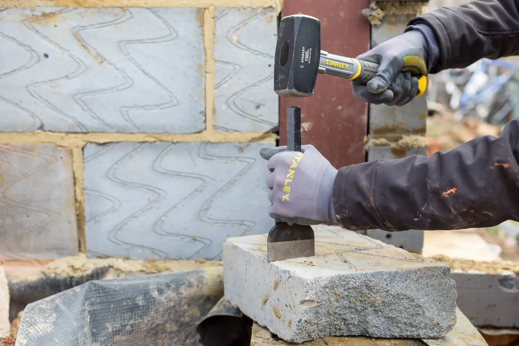 Photo of STANLEY STHT0-54128 sledge hammer in use, striking a chisel on a concrete block at a construction site.