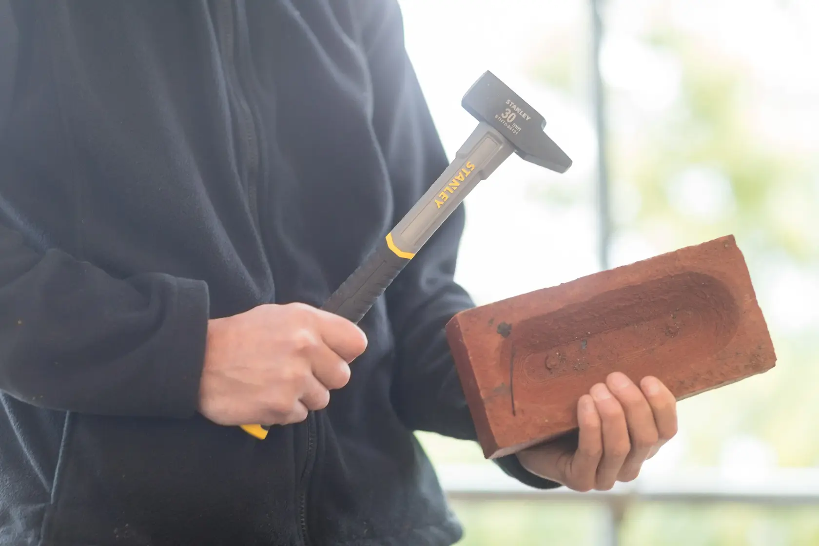 Photo of STANLEY STHT0-54131 club hammer with yellow handle held near a red brick.