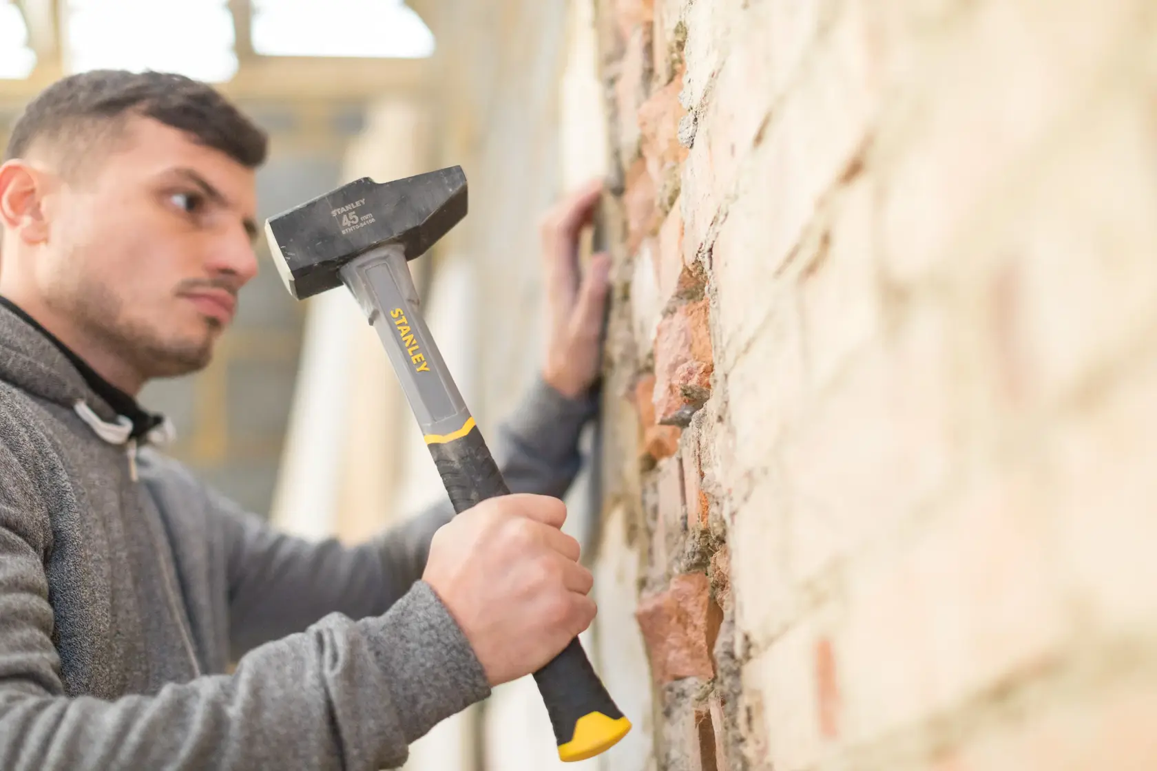Stanley STHT0-54156 club hammer with black and yellow handle used on brick wall, angled side view.