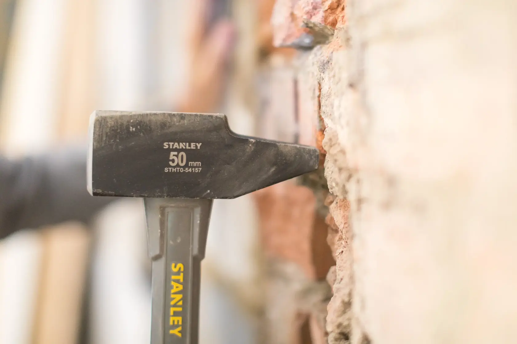 Stanley STHT0-54157 hammer in use against brick wall, close-up side angle, yellow branding visible.