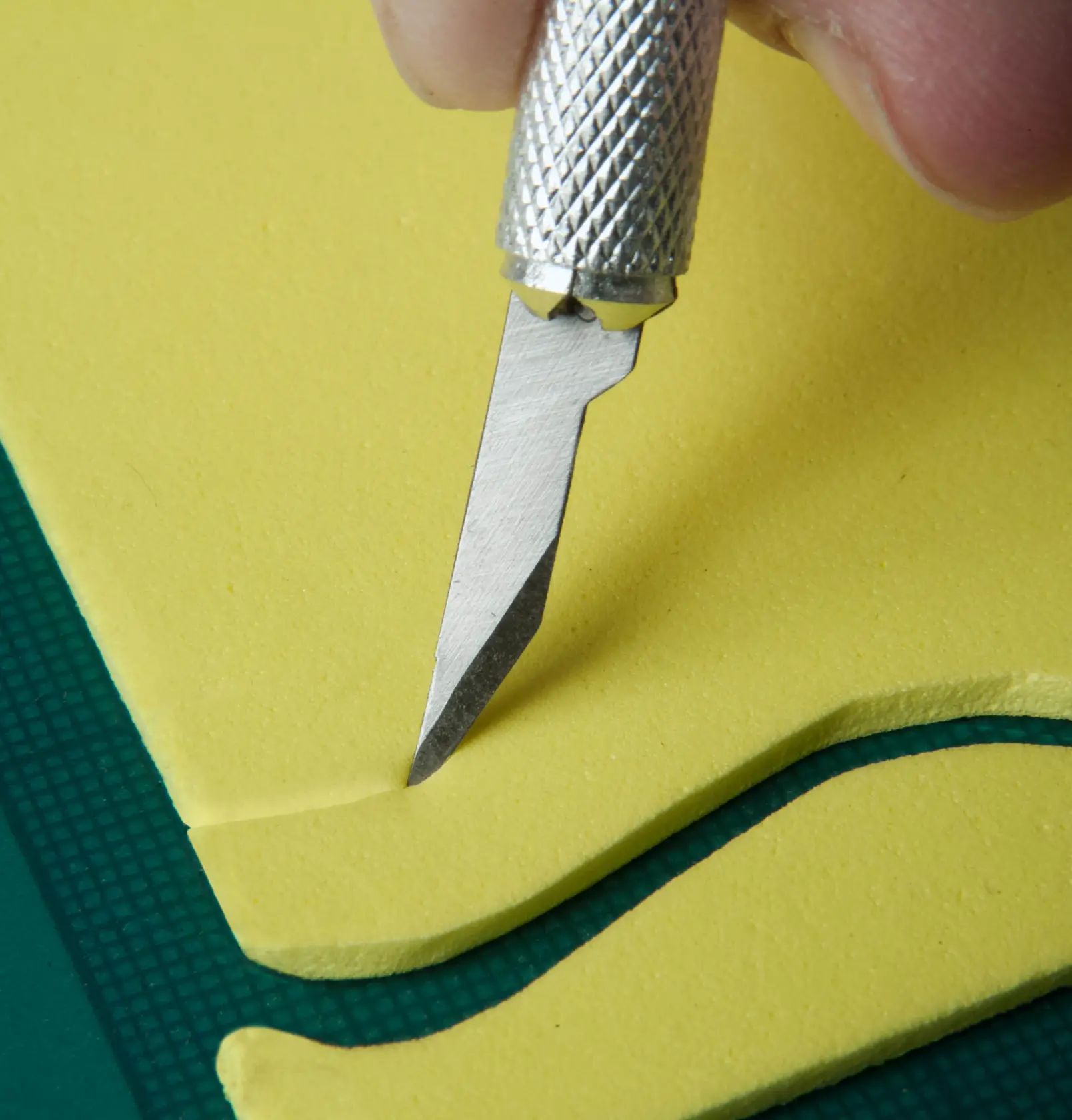 STANLEY STHT0-73872 precision craft knife cutting yellow foam on green surface, close-up angle.