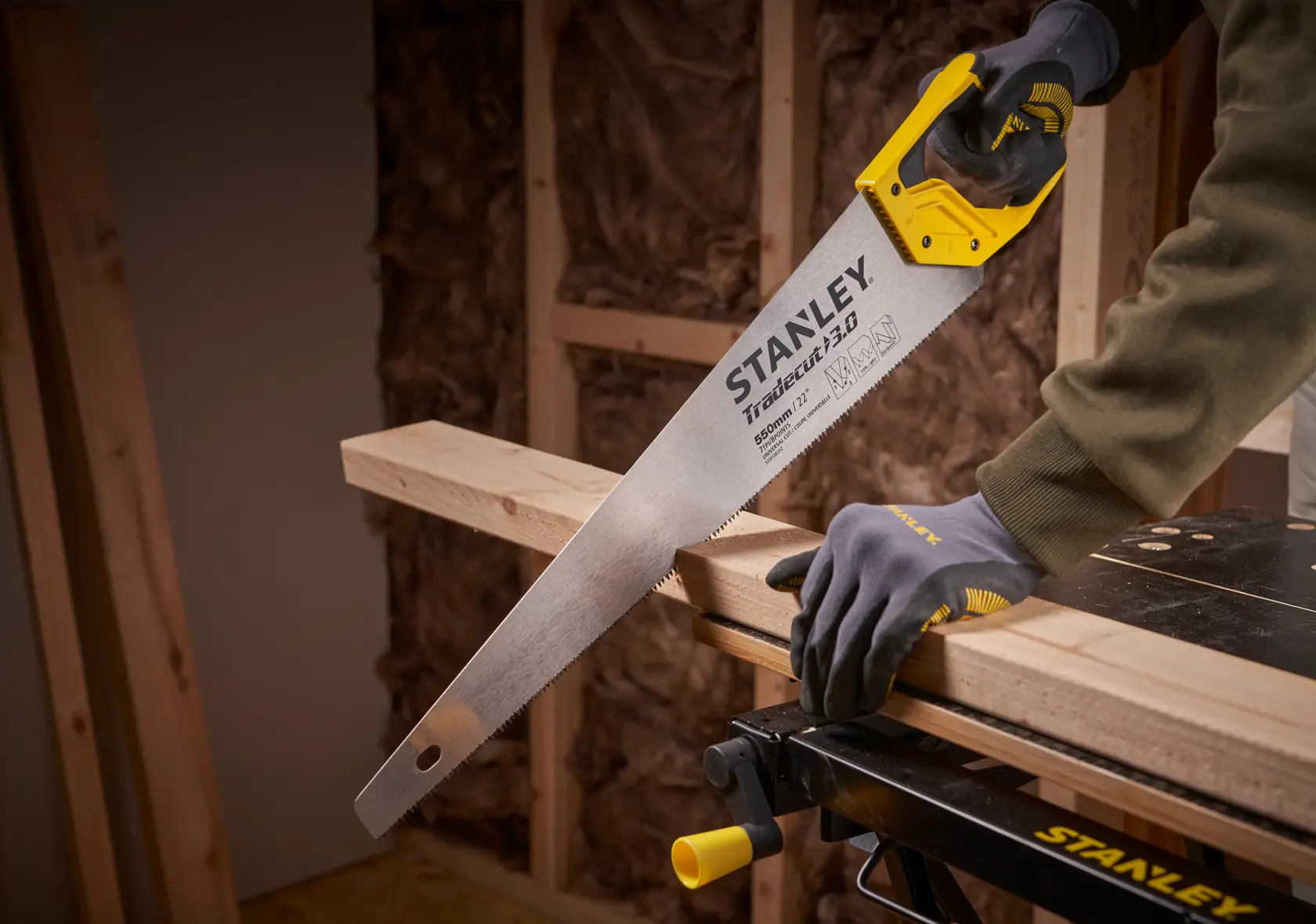 STANLEY STHT1-20352 hand saw with yellow handle cutting wooden beam in workshop setting.