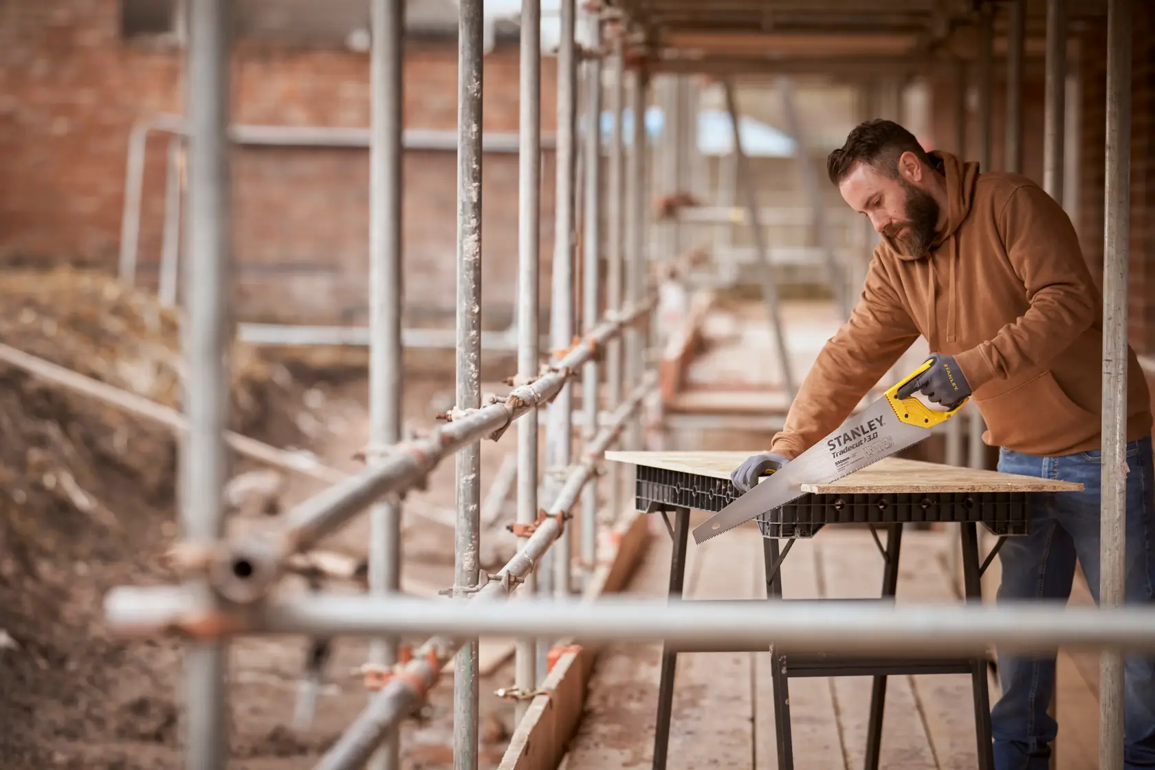 STANLEY STHT1-20352 hand saw in use on a construction site, cutting wood on a sawhorse table.