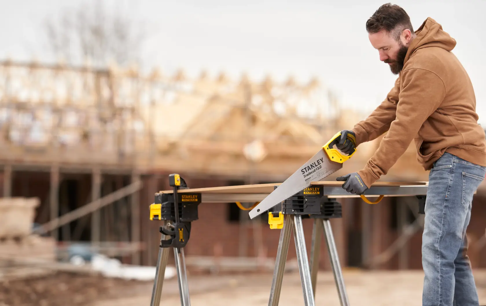 STANLEY STHT1-20352 hand saw used outdoors on a construction site, cutting wood on a workbench.