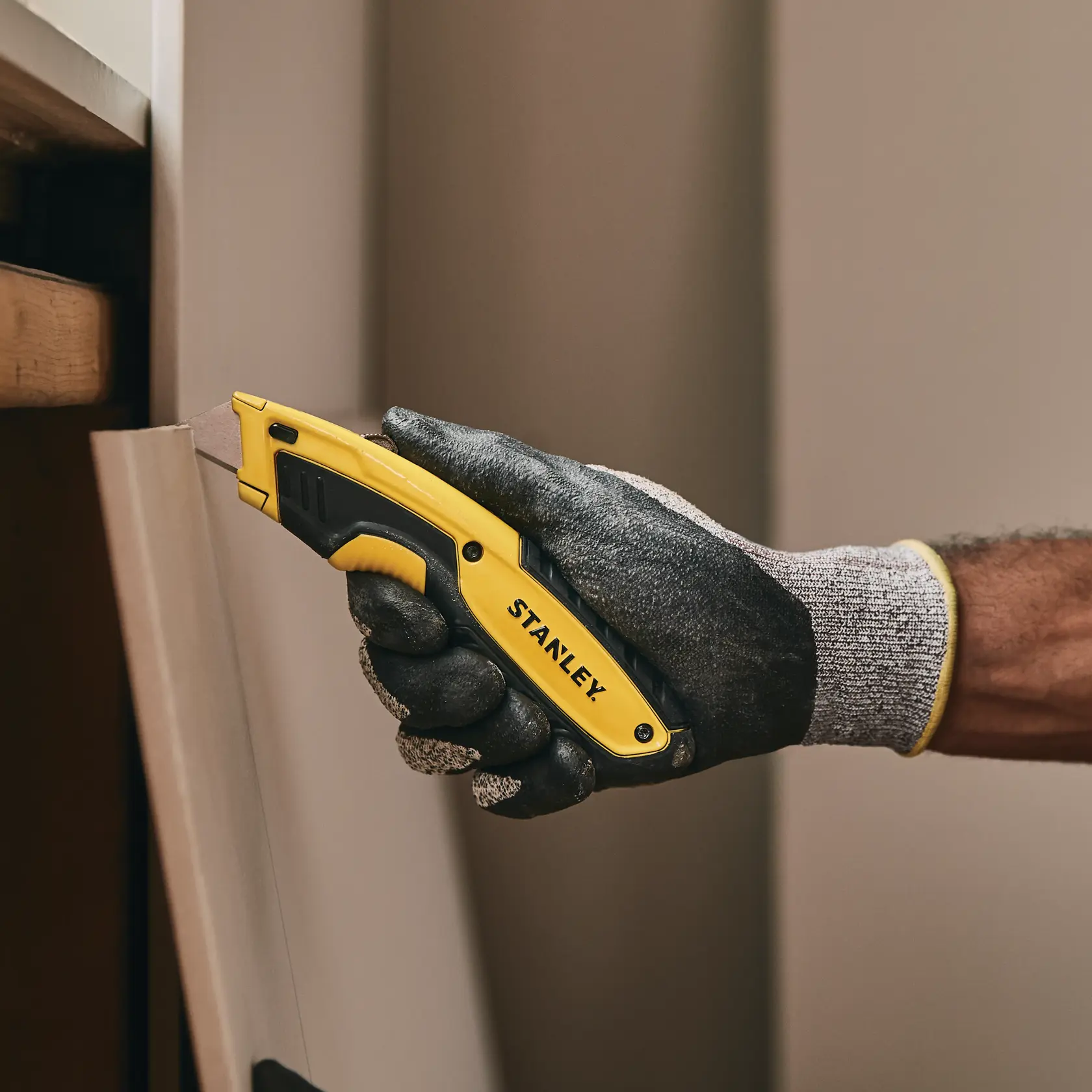 Stanley STHT10479-0 Cuttermesser in behandschuhter Hand beim Schneiden eines Panels. Kategorie Fotografie.
