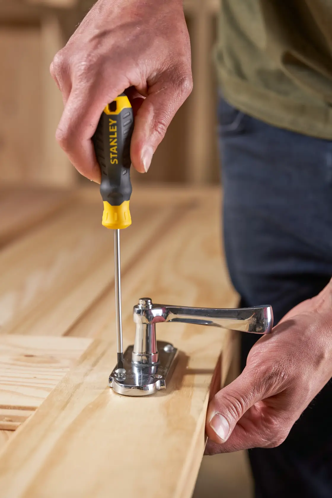STANLEY STHT16195-0 screwdriver with black and yellow handle used to fasten a hinge on a wooden surface.