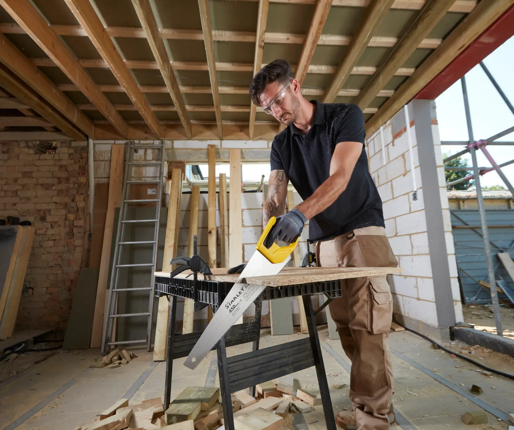 STANLEY STHT20354-1 hand saw with yellow handle in use cutting wood on a construction site.