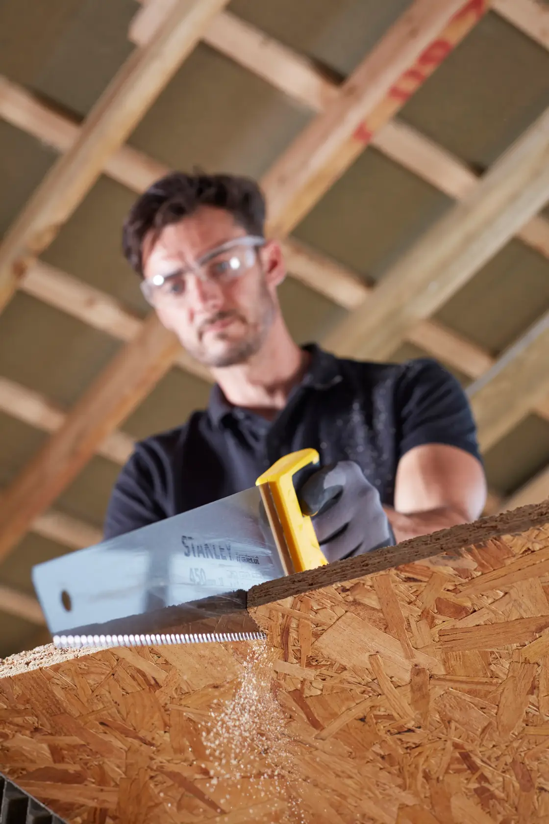 Photo of STANLEY STHT20354-1 handsaw cutting wood panel, close-up showing sawdust and yellow handle.